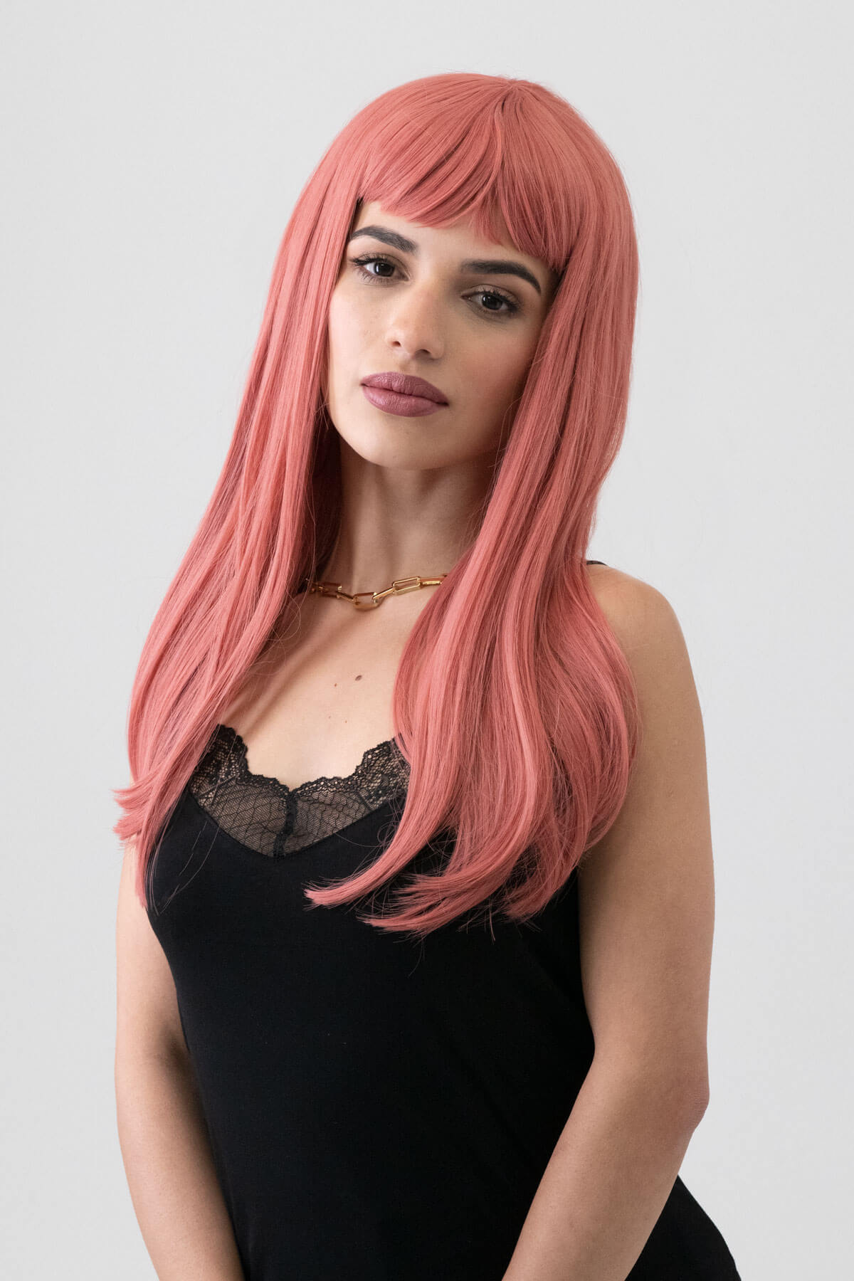 Woman with long pink wig wearing a black top against a plain background. Long Pink Wig With Short, Straight Fringe: Stephanie