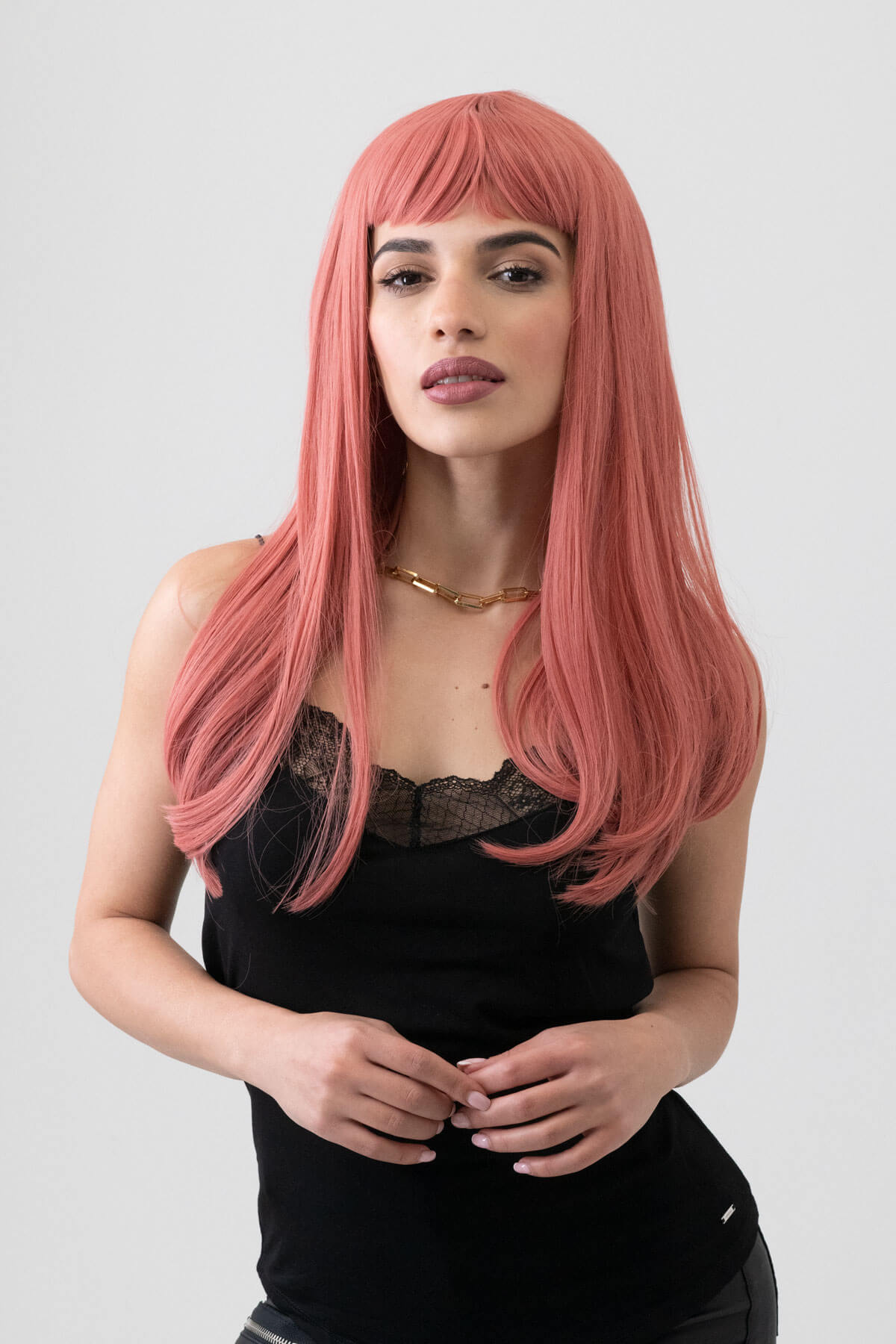 Woman with long pink wig wearing a black top on a plain background. Long Pink Wig With Short, Straight Fringe: Stephanie
