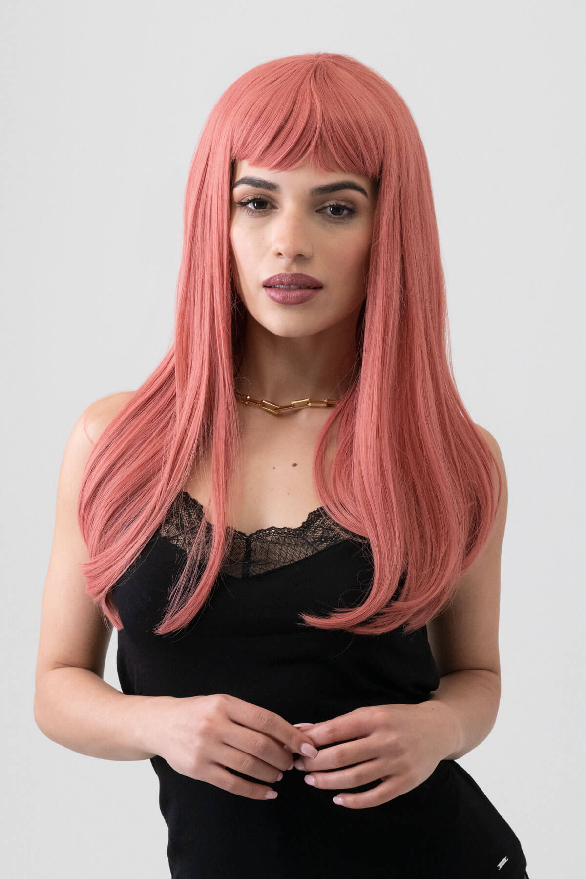 Woman with long pink wig wearing a black top against a plain background. Long Pink Wig With Short, Straight Fringe: Stephanie