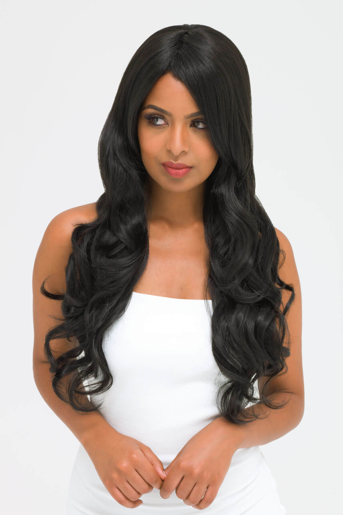 Woman with long black wavy hair wearing a white top on a light gray background. Long wavy black wig with side-sweeping Fringe: Charlotte