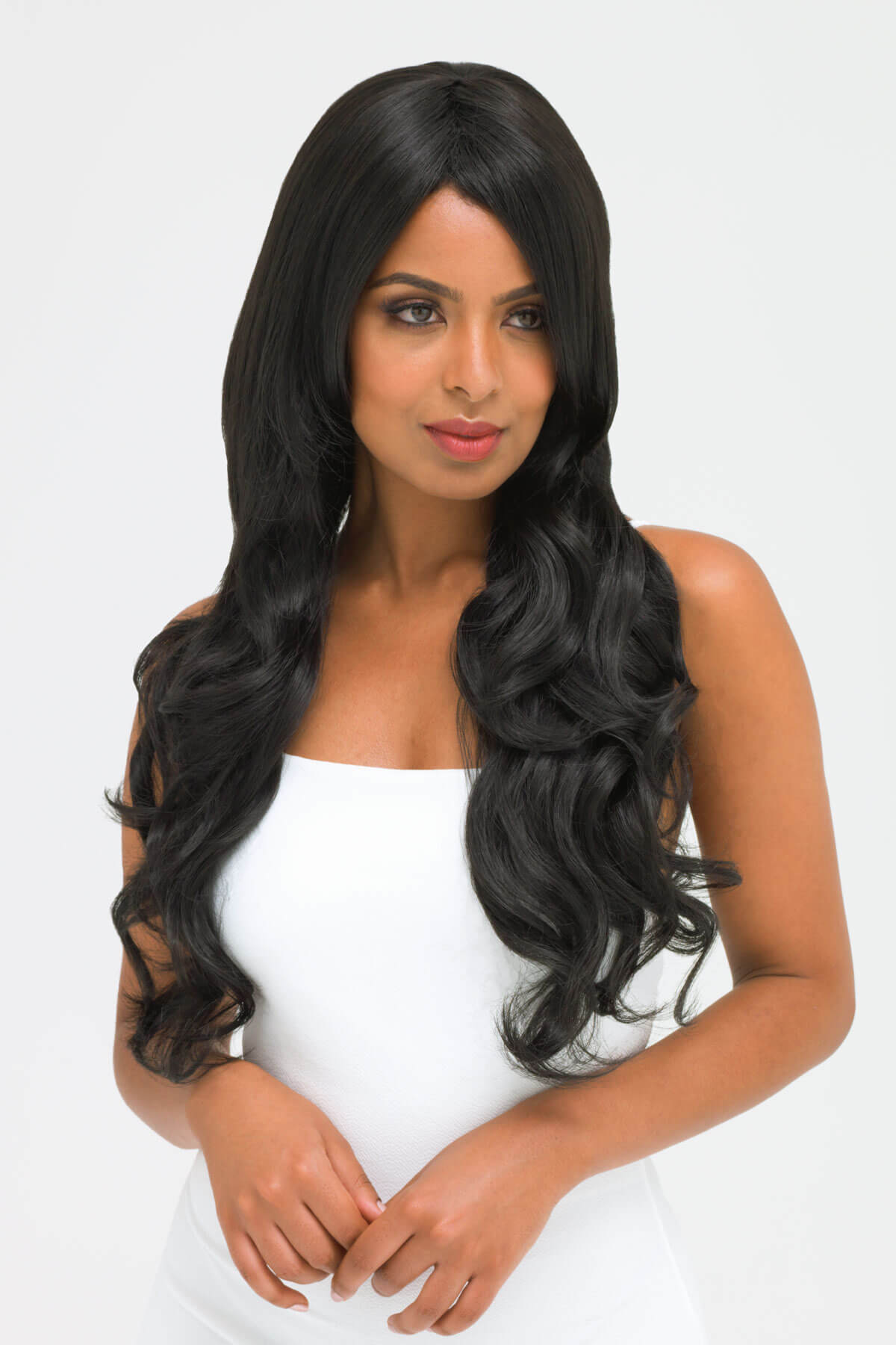 Woman with long black wavy hair wearing a white top on a light gray background. Long wavy black wig with side-sweeping Fringe: Charlotte