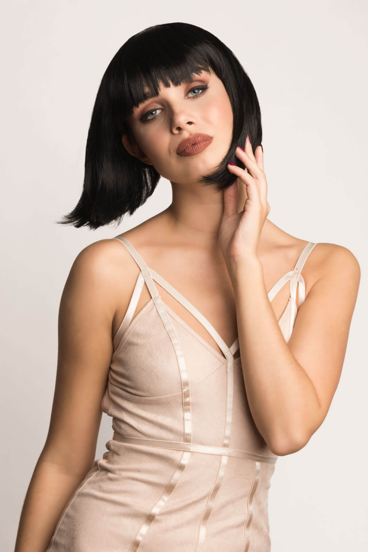Woman wearing a beige dress with thin straps against a plain background. Black inverted bob wig: Chloe