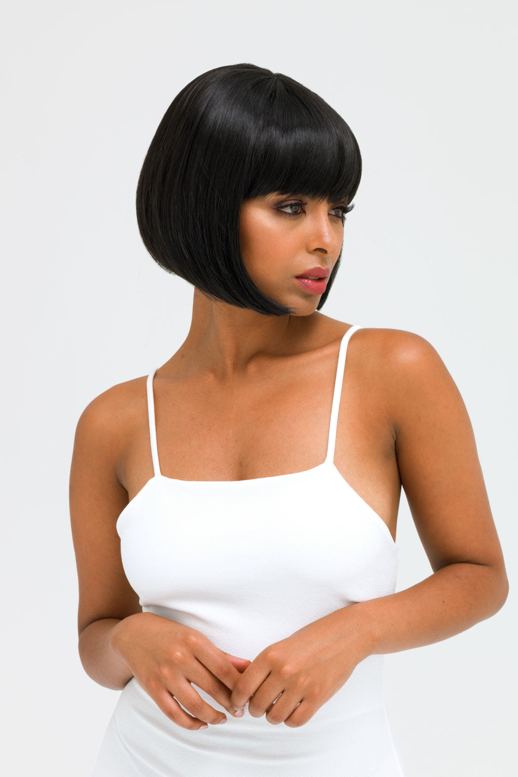 Woman wearing a white top with a plain background. Short black bob wig: Josie