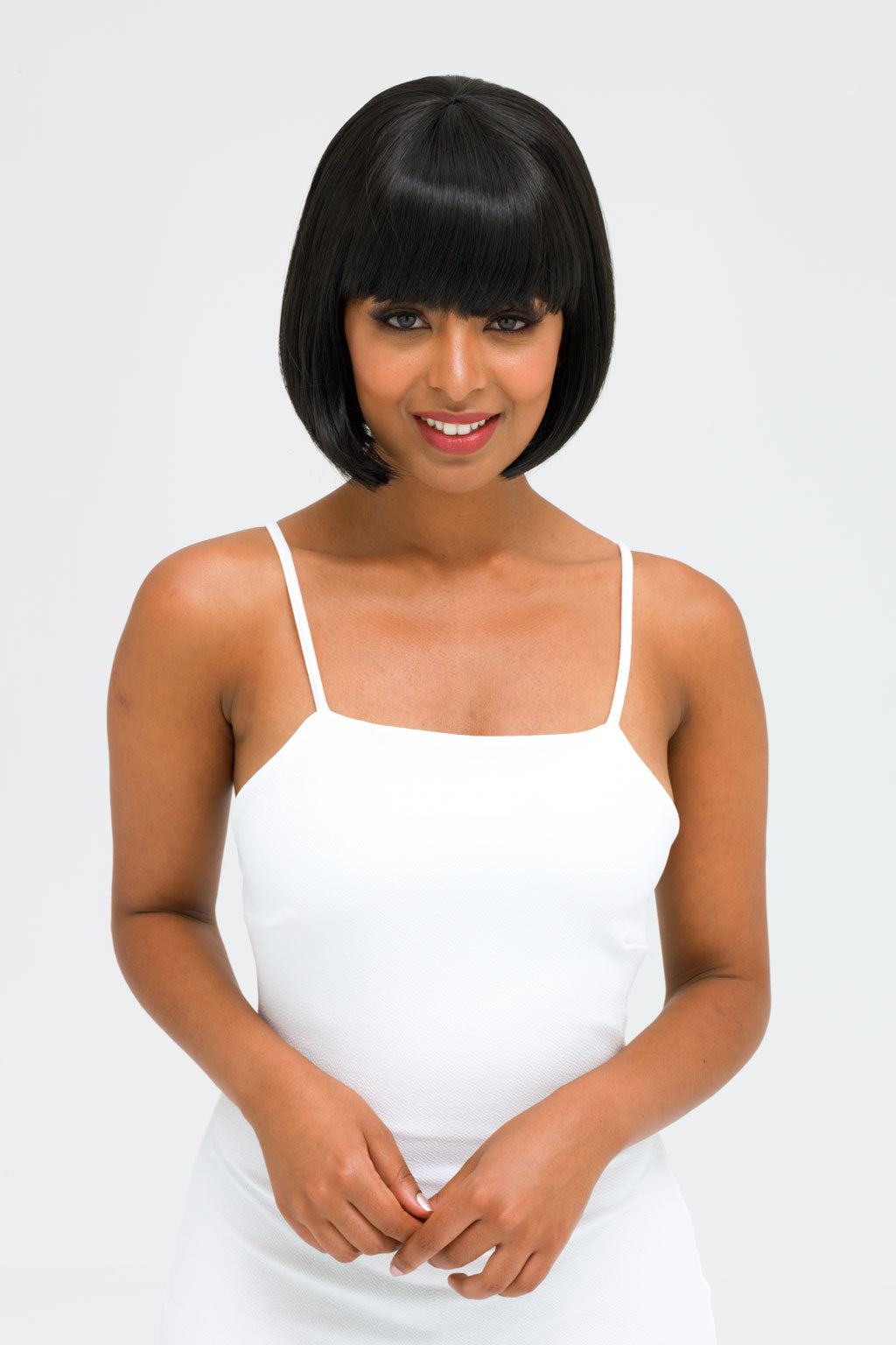 Woman wearing a white spaghetti strap dress against a plain background. Short black bob wig: Josie