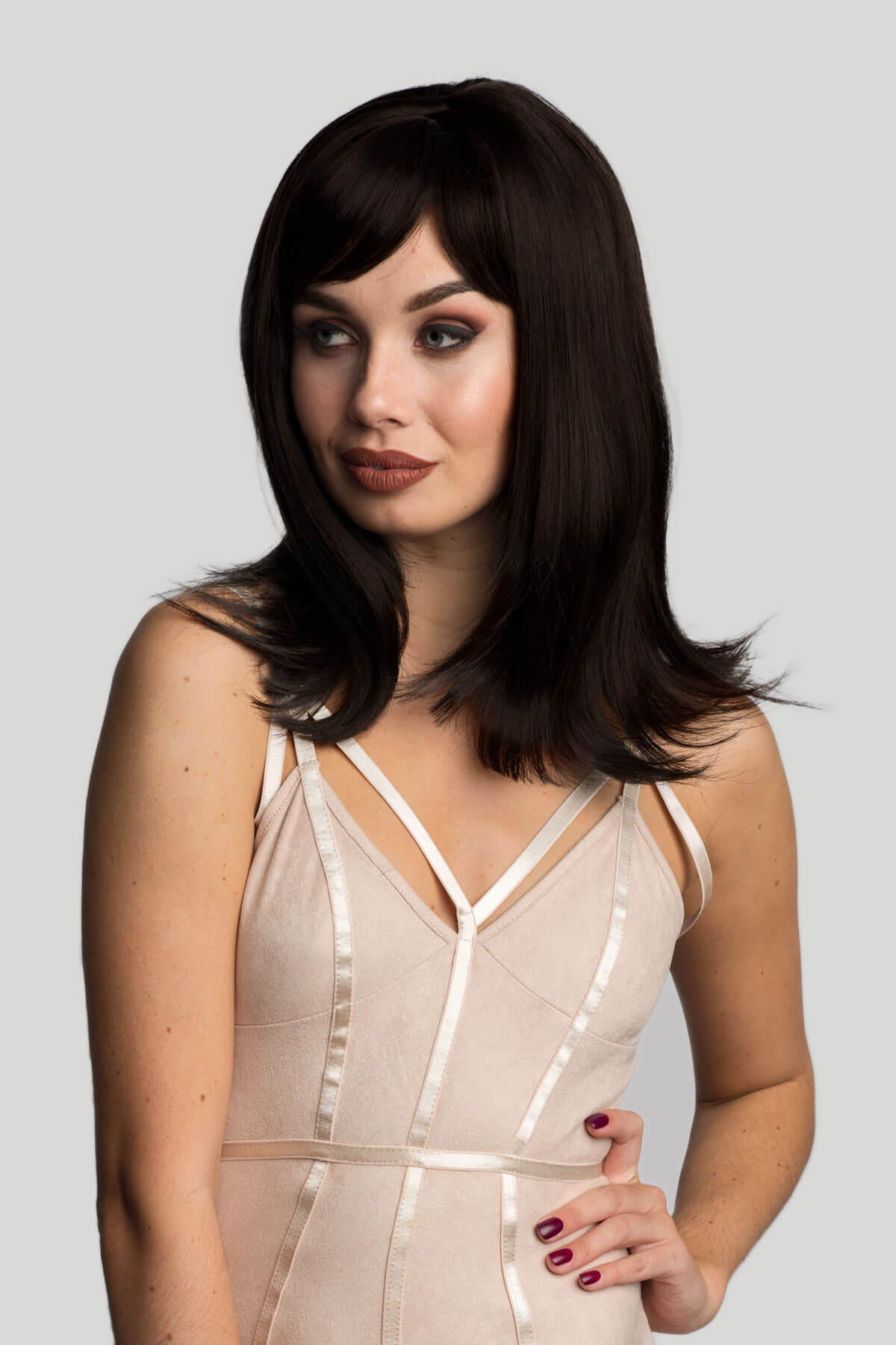 Woman wearing a beige dress with a plain background. Brown long bob wig, layered with straight fringe: Katia dark brown 2