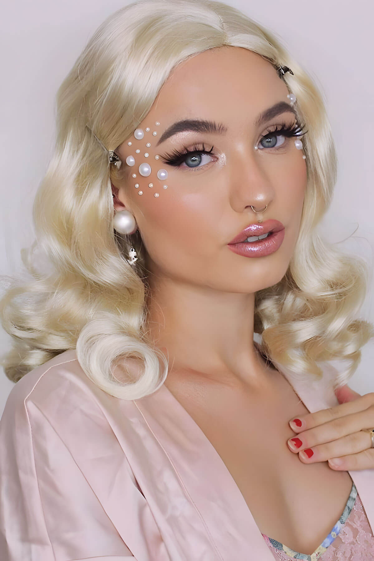 Woman with blonde hair and makeup wearing a pink robe against a white background. 40s blonde pinup style wig with marcel waves: Lauren