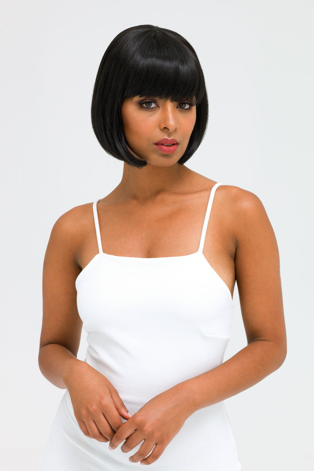 Woman wearing a white spaghetti strap dress against a plain background. Short black bob wig: Josie