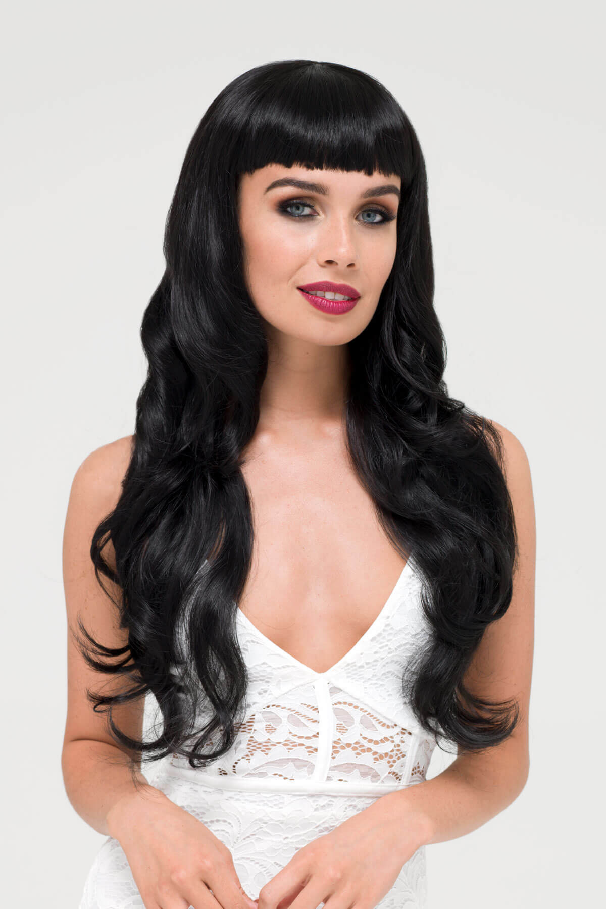 Woman with long black wig and white lace top on a light gray background. Long wavy black wig with vintage-style, rockabilly, straight fringe: Eloise