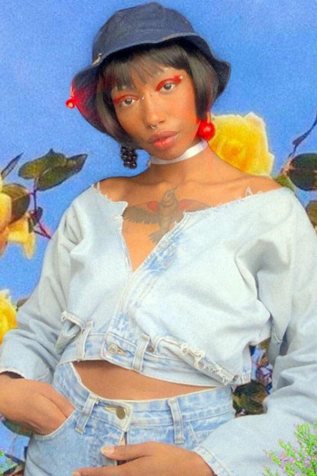 Person wearing a denim outfit with flowers and a blue background. Louise Brooks style wig, short black bob: Brooks