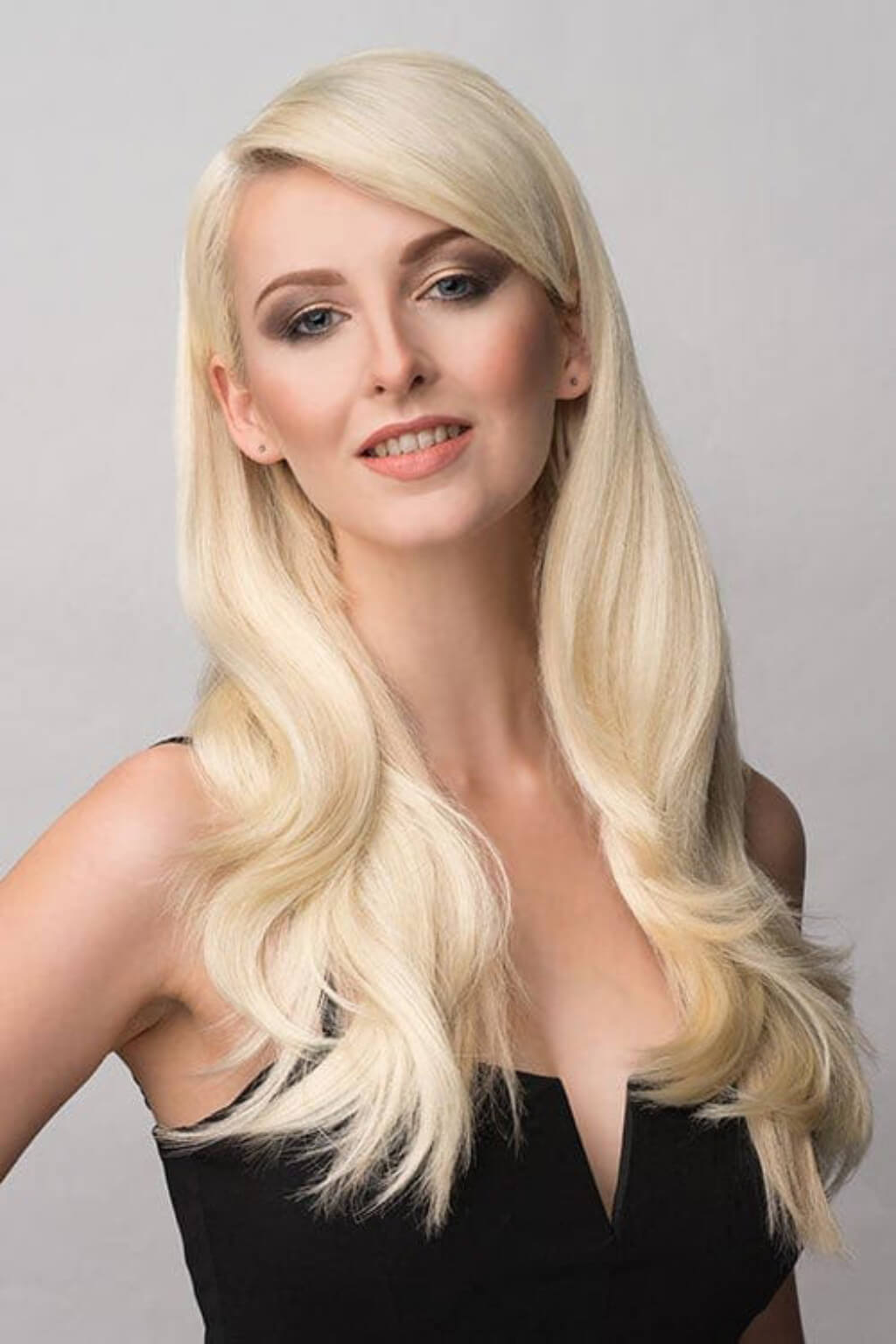 Woman with long blonde hair against a grey background. Straight blonde half wig hairpiece (3/4 wig), layered: Autumn blonde 613