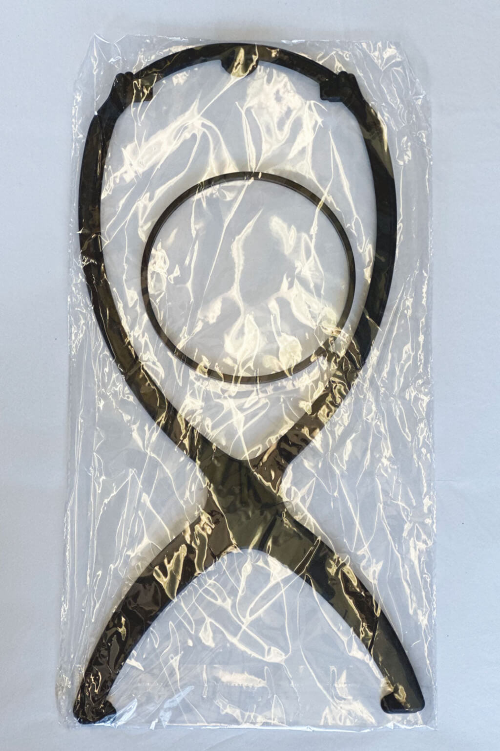 Black metal tool in clear plastic packaging on a white background. A collapsible wig stand - black