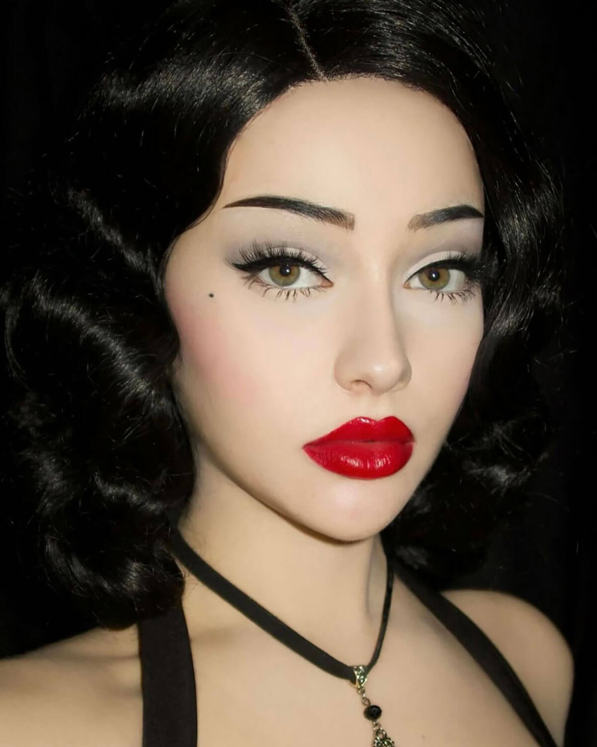 Close-up of a person with dark hair and red lipstick against a black background. Black lacefront wig, pinup/vintage style, mid length with finger waves: Etta