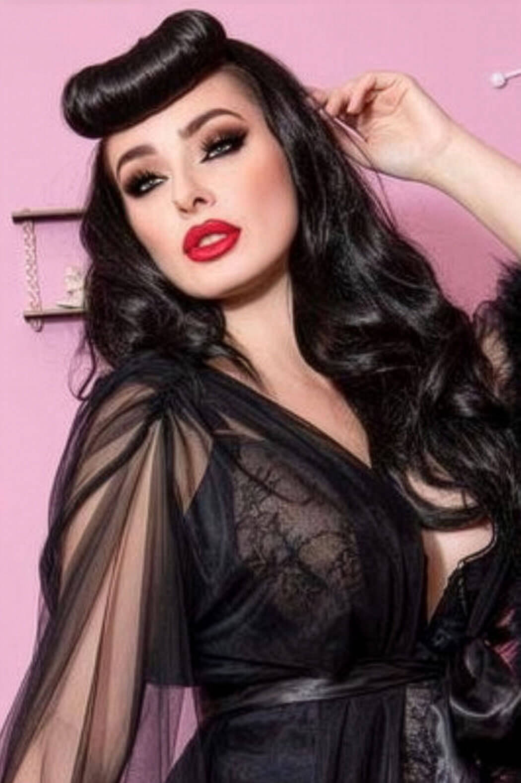 Woman in a black lace dress with sheer sleeves against a pink background. Bumper bangs pack - vintage 40s 50s fringe roll: Lena black 1B