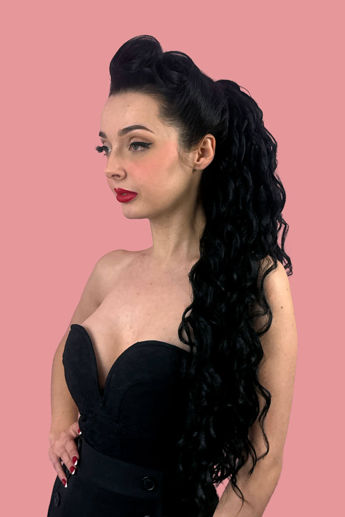A woman in profile wearing a black strapless dress, showcasing a long, dark, curly wavy hair extension against a solid pink background. Long Curly Ponytail Hair Piece Extension, Black