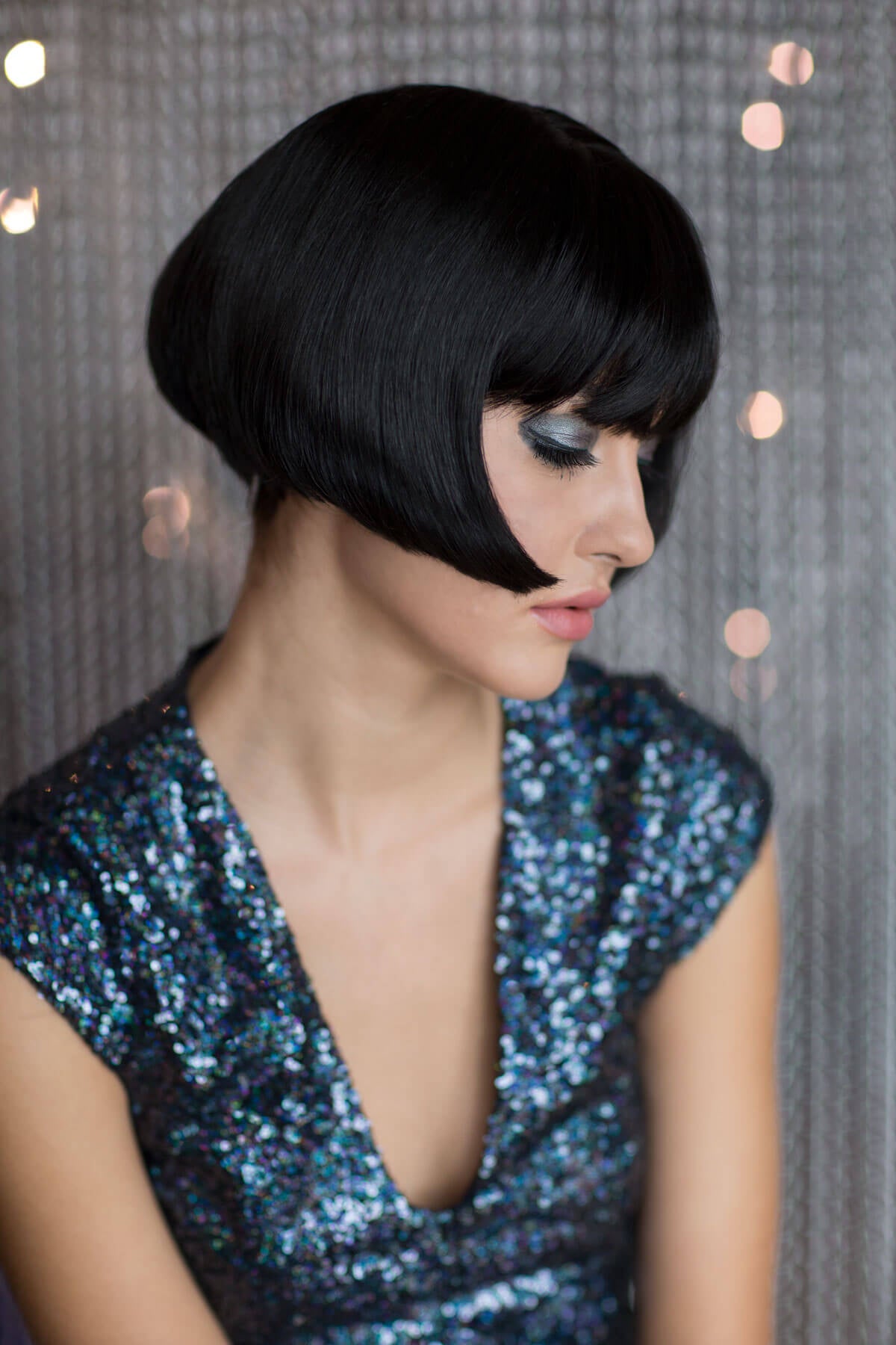 Woman with a stylish black bob haircut wearing a sequined dress against a textured wall. Louise Brooks style wig, short black bob: Brooks