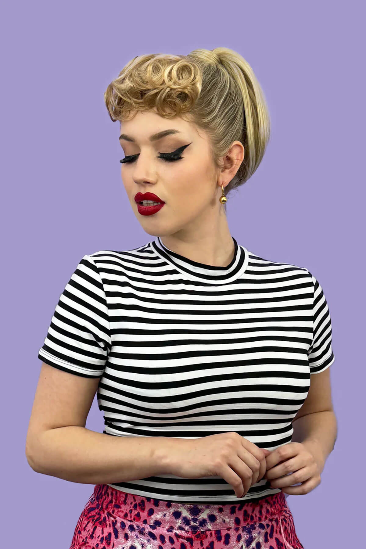 Woman wearing a black and white striped shirt against a purple background. Curly 1940s style clip-in fringe hairpiece/clip-in bangs: Bunny ash blonde 24 