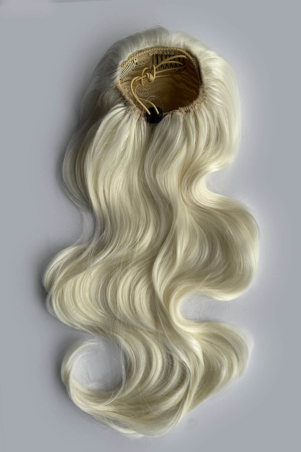 A long, wavy wig in a platinum blonde colour with a draw string attachment, displayed against a solid grey background. Double volume hairpiece extension: Naomi platinum blonde 1001