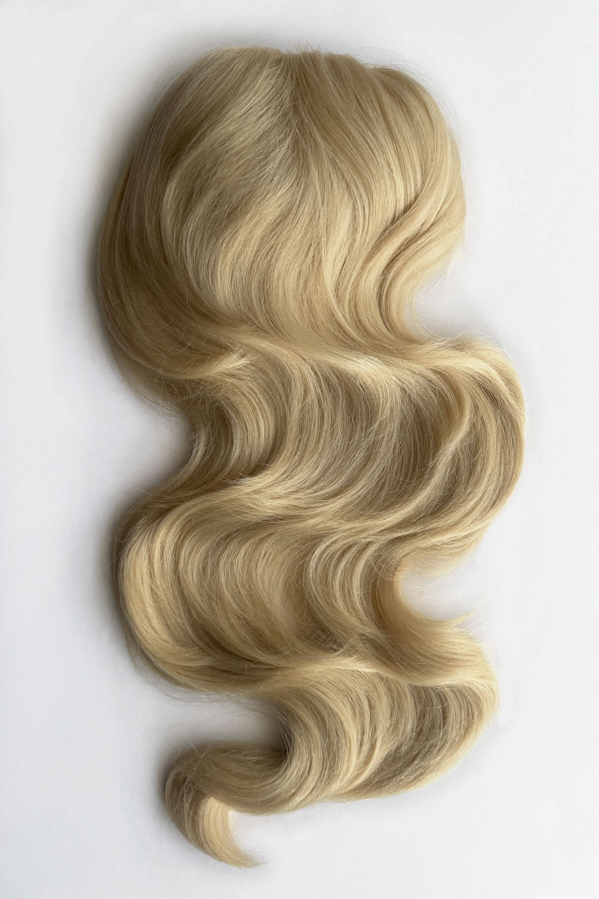 A wavy blonde hair piece, styled in voluminous curls, shown against a plain background. Double volume hairpiece extension with gentle waves: Naomi blonde 613