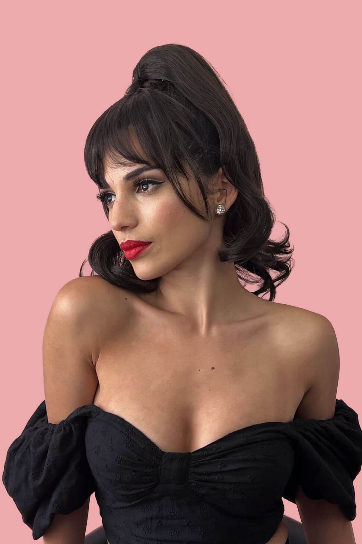Woman wearing a black off-shoulder top against a pink background. Clip in fringe hairpiece/clip-in bangs, gently feathered with face framing whisps: Delia dark brown 4