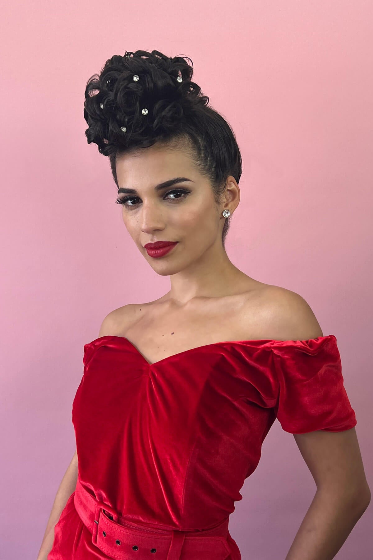 Woman in a red off-shoulder dress with a pink background. Hair poodle clip-in hairpiece bun vintage style 1950s: Lucille jet black 1