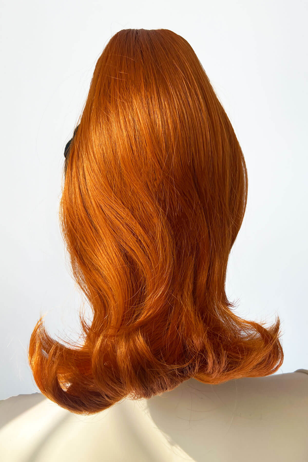 Red wig on a mannequin head against a white background. Ponytail hairpiece, shoulder length with flick/flip, retro 1960s style: Ariana Ginger