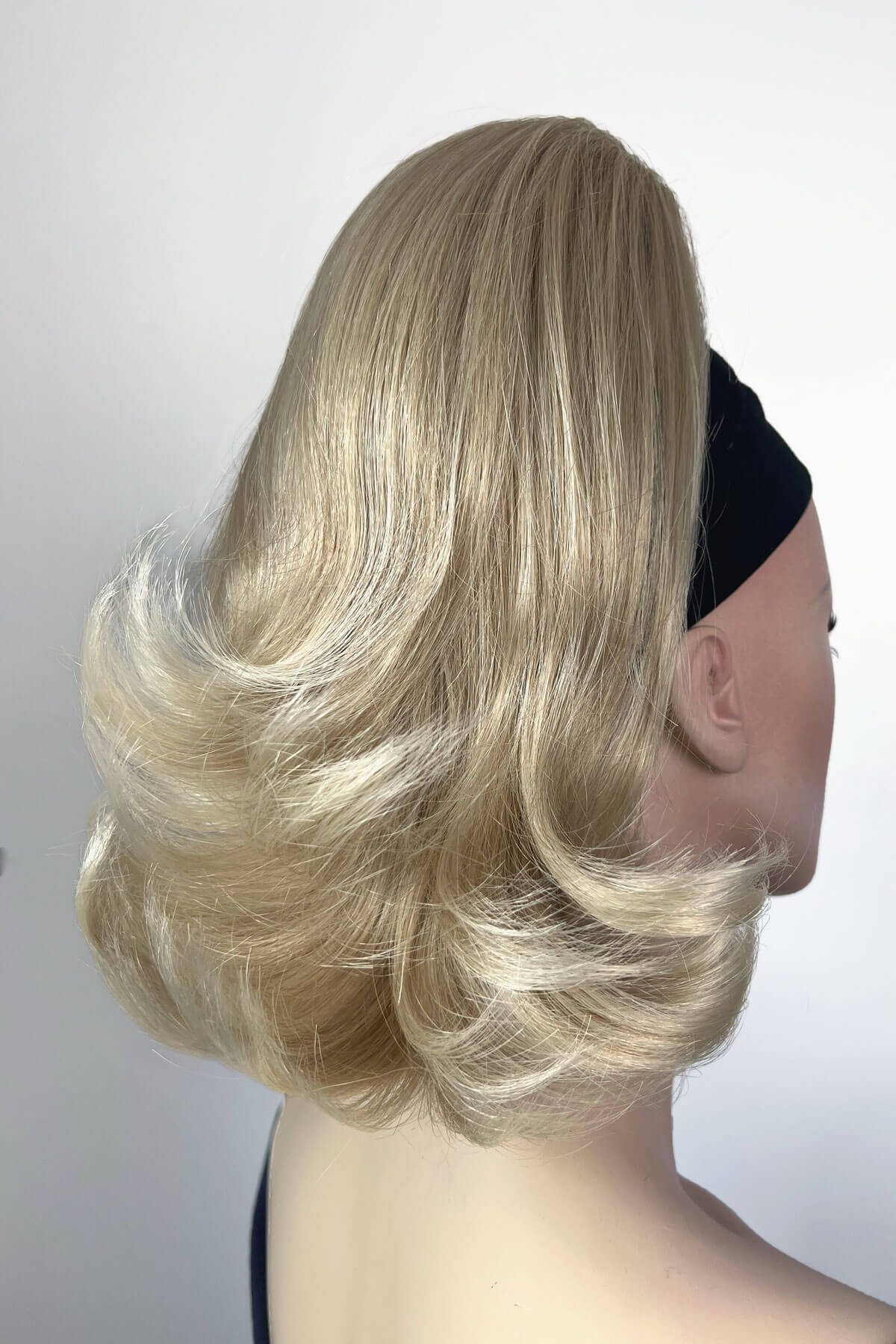 Blonde wig on a mannequin head against a white background. Ponytail hairpiece, shoulder length with flick/flip, retro 1960s style: Ariana blonde 613T24
