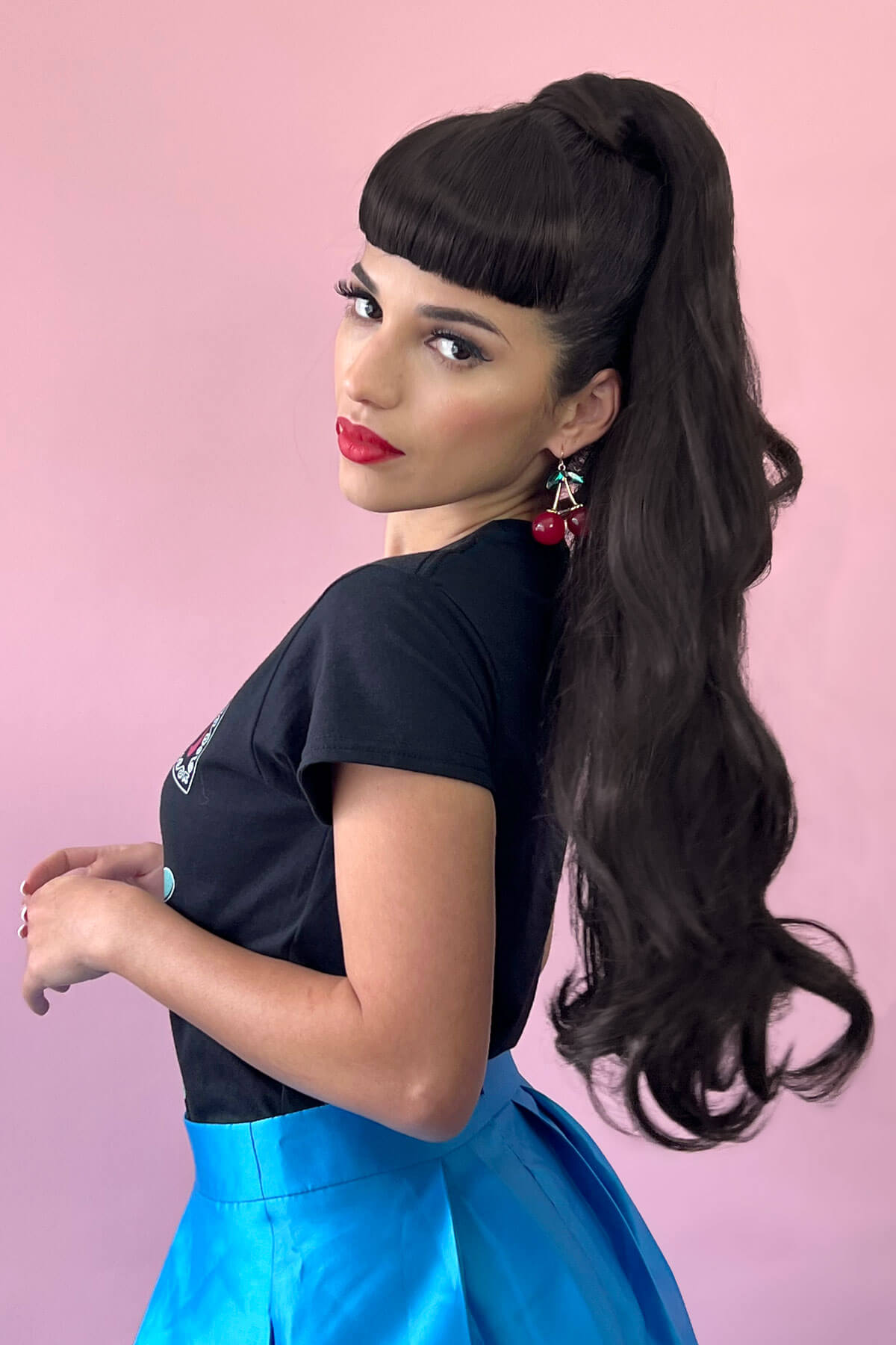 Woman with long dark hair styled in a high ponytail against a pink background.Long ponytail extension  with soft waves: Sophie 613T24