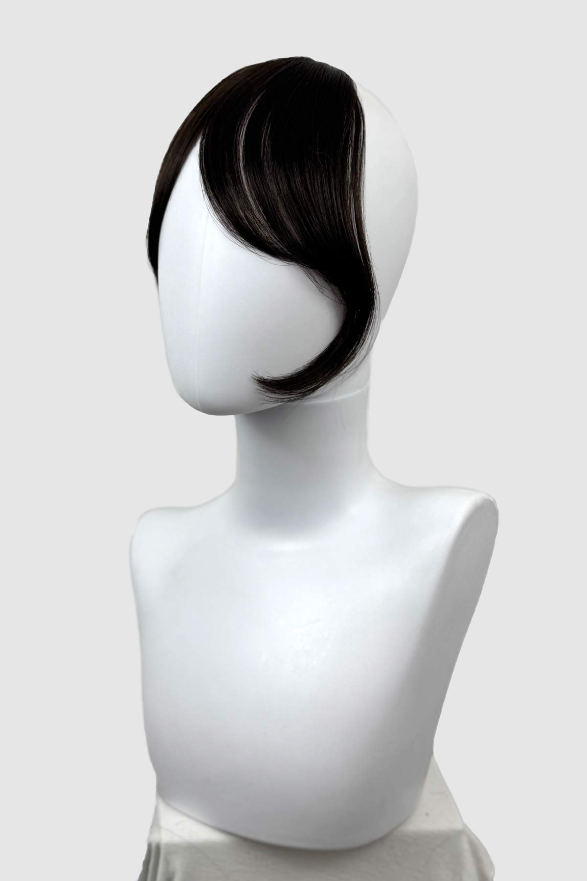 Mannequin head with a black hairpiece on a white background. Clip in fringe hairpiece/clip-in curtain bangs, with long, face framing wisps: Sabrina dark brown 4