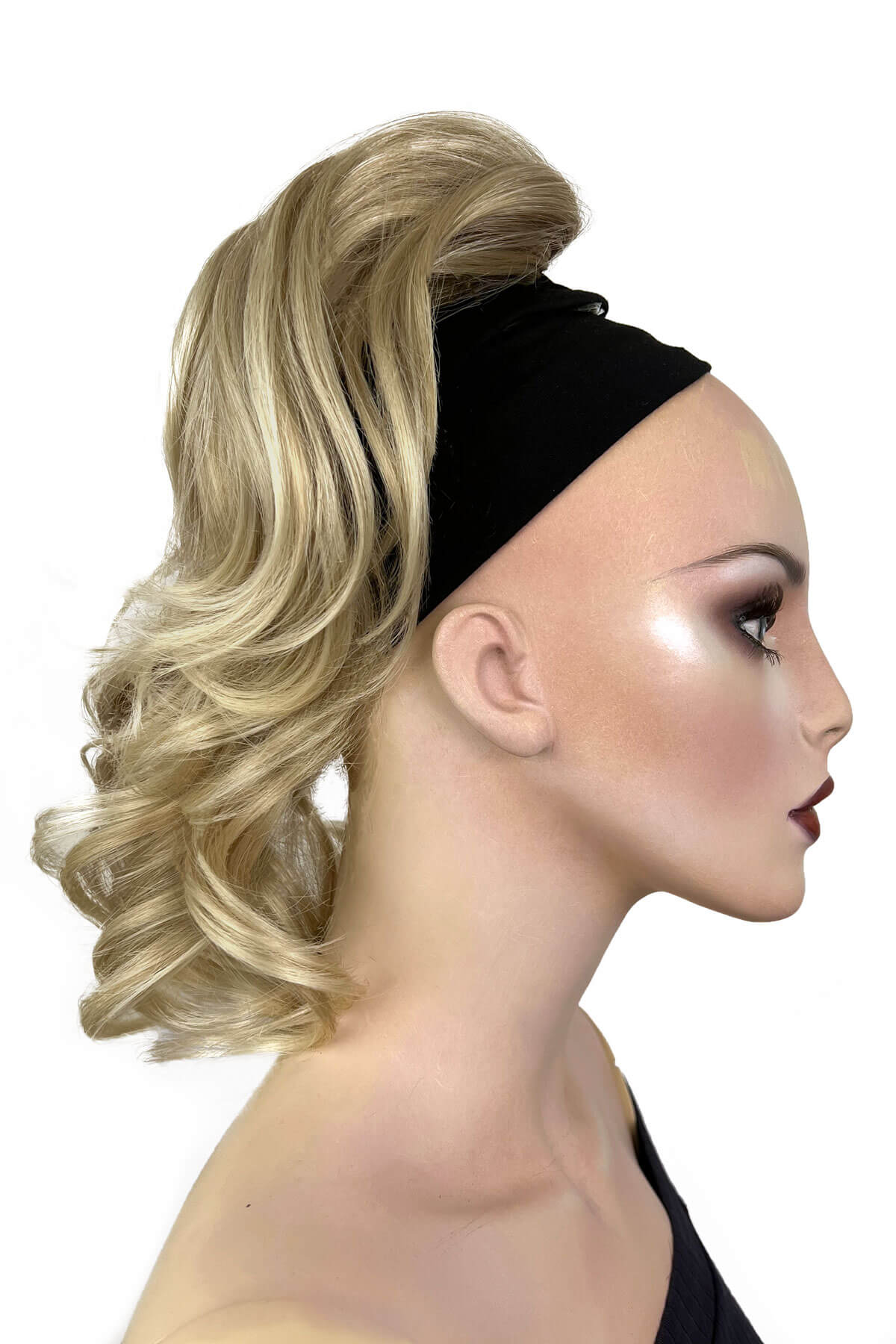 A woman wearing a curly ponytail extension hairpiece with loose, layered curls. She is seen from the shoulders up. Curly ponytail extension clip-on hairpiece: Tulisa blonde 613T24