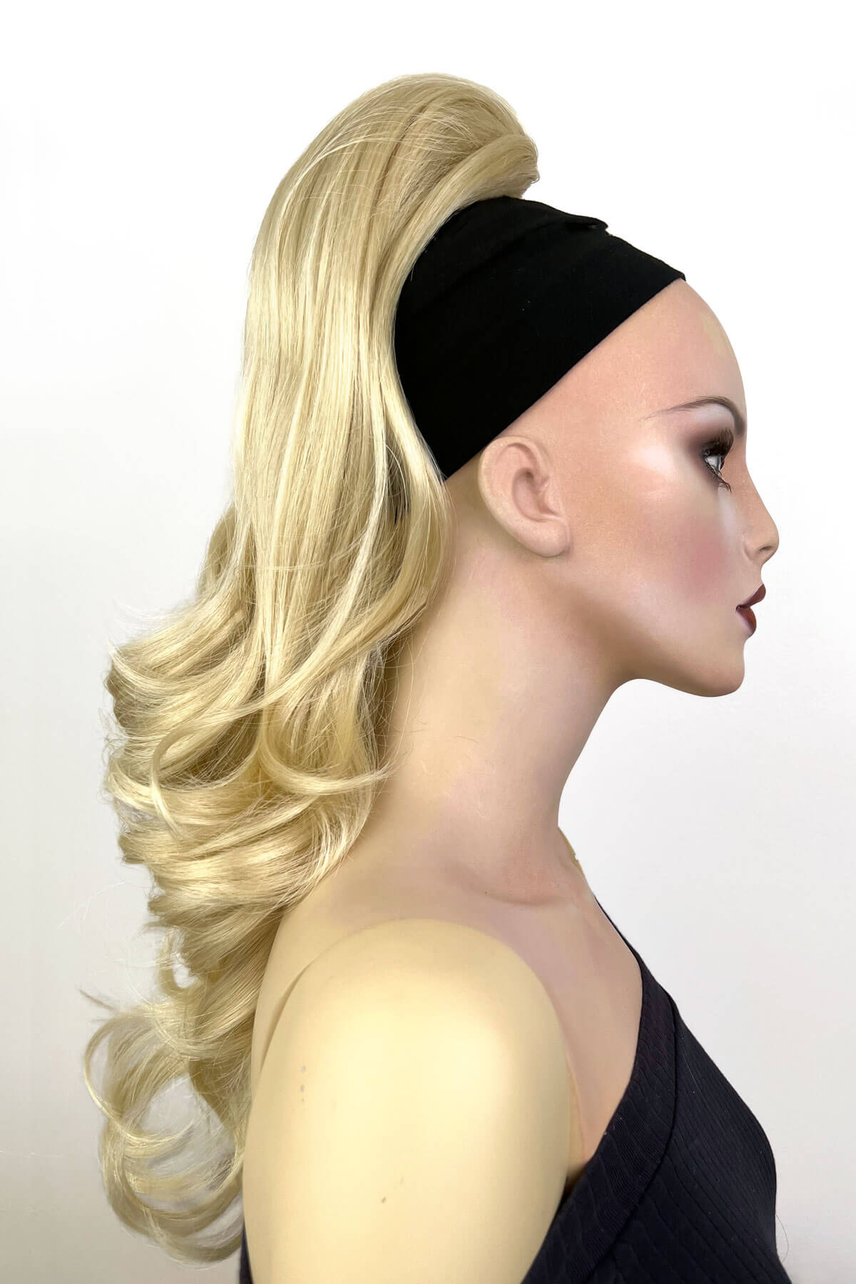 Mannequin head with long blonde hair styled in a ponytail wearing a black headband against a white background. Wavy, long ponytail hairpiece extension: Casey champagne blonde 613
