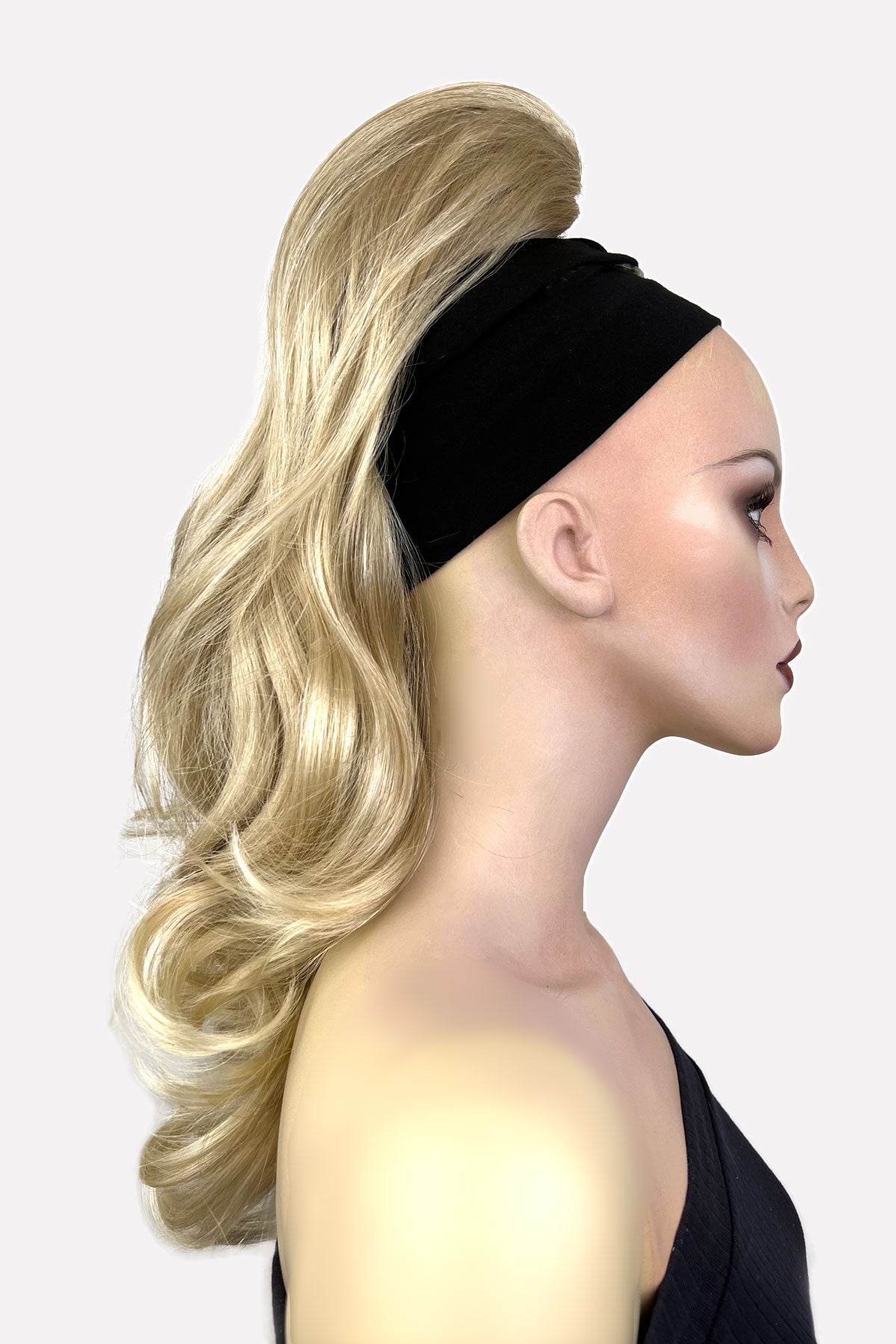 Woman wearing a black headband with blonde hair styled in an elegant updo on a white background. Wavy, long ponytail hairpiece extension: Casey blonde 613T24