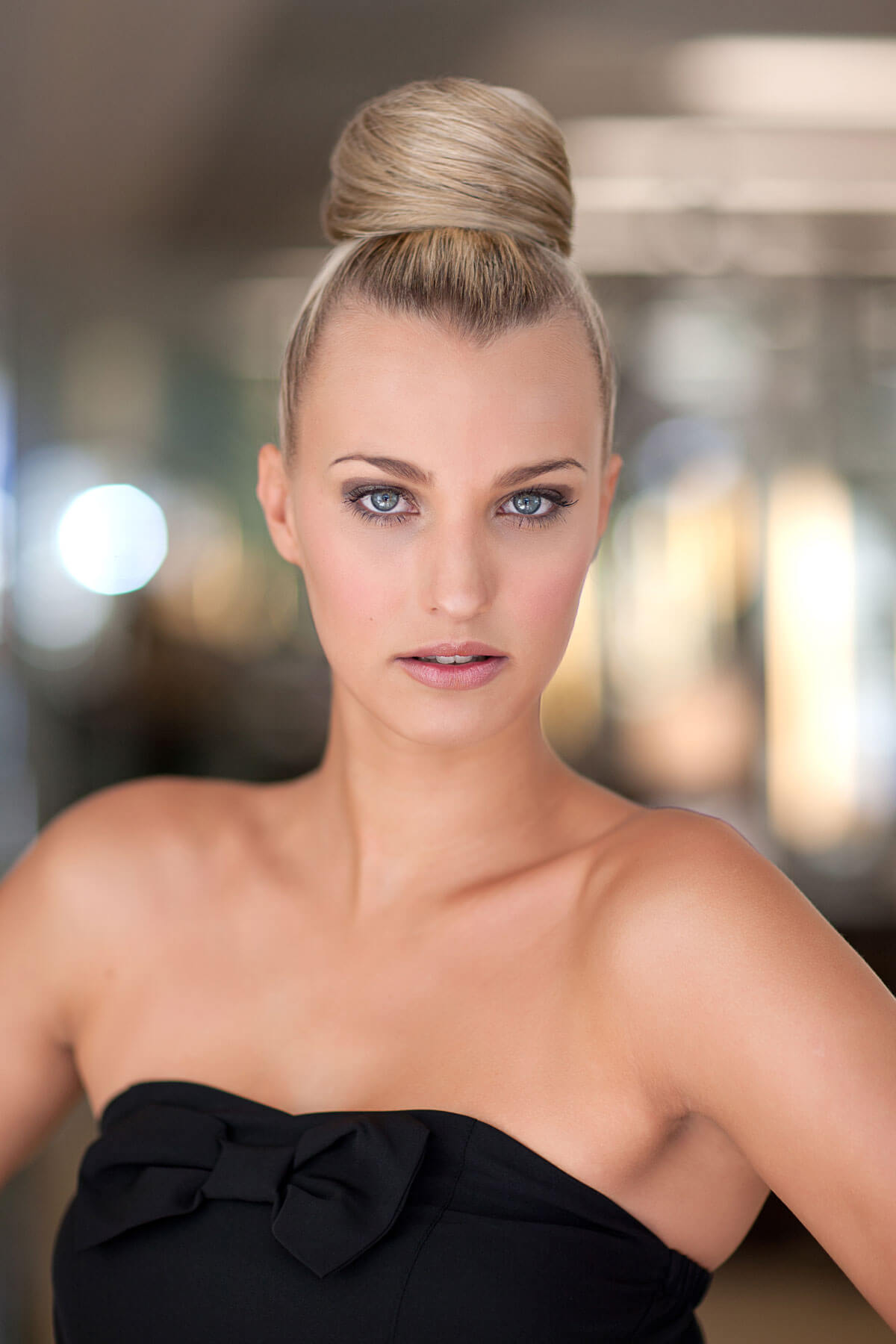 Woman with a styled hairbun wearing a black strapless dress against a blurred background. Hair bun hairpiece; instant perfect hairbun: Hebe