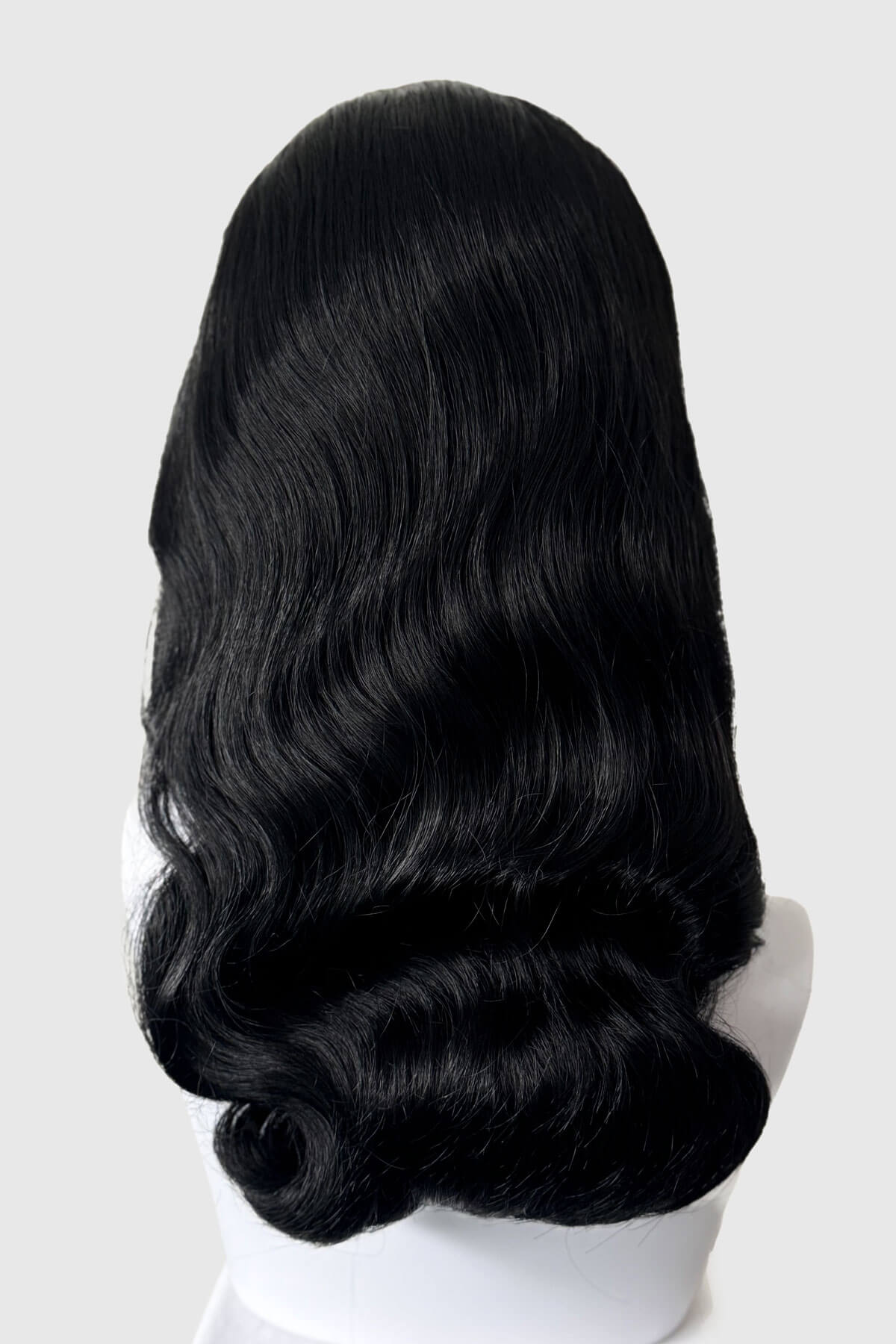 Black wig on a white mannequin head against a light gray background. 1950s style half wig hairpiece with beautiful waves: Morgana jet black 1