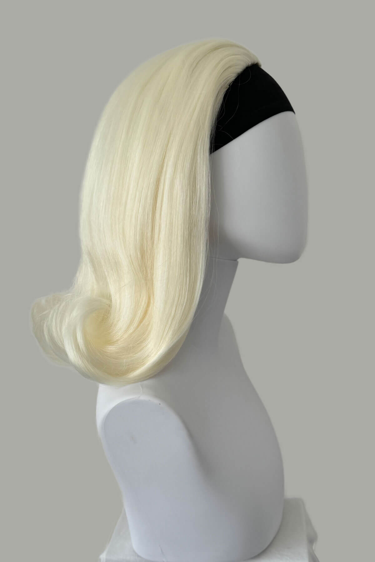 Blonde wig on a mannequin head against a gray background. 1960s half wig hairpiece, flicked, hair flip: Philippa Platinum blonde 1001