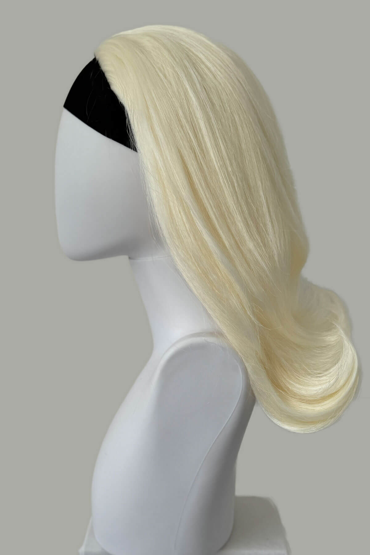 Blonde wig on a mannequin head against a gray background. 1960s half wig hairpiece, flicked, hair flip: Philippa Platinum blonde 1001