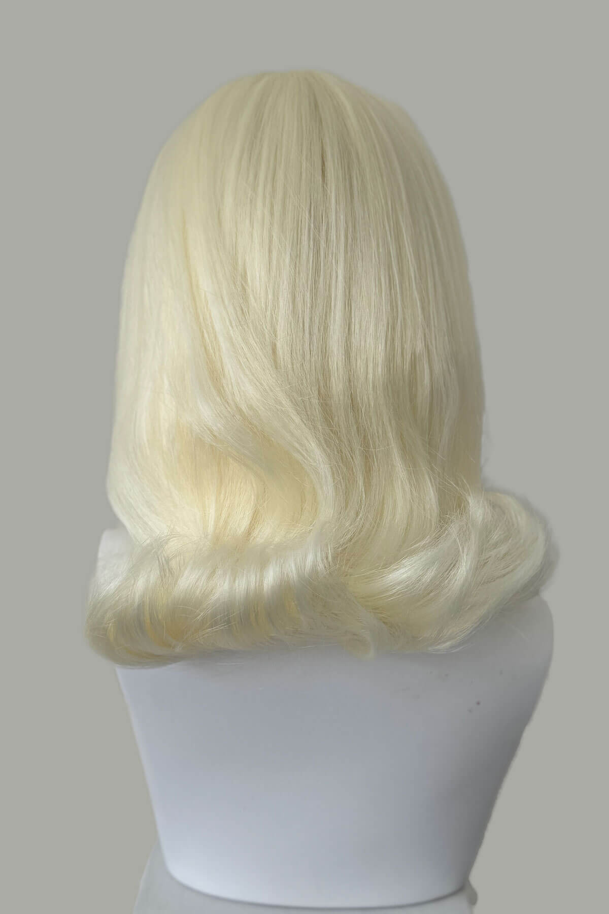 Blonde wig on a mannequin head against a plain background. 1960s half wig hairpiece, flicked, hair flip: Philippa Platinum blonde 1001