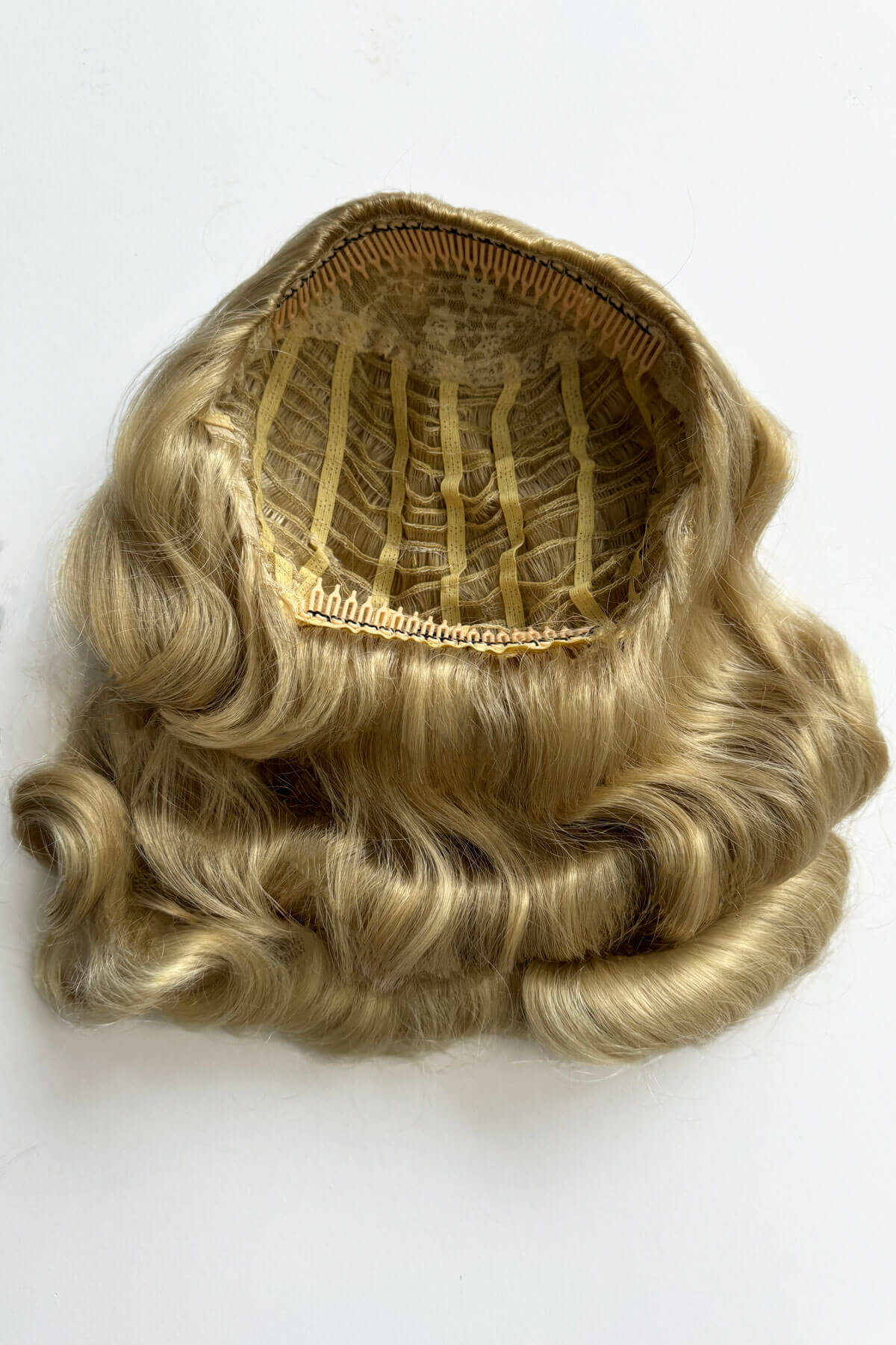 Blonde hairpiece with a mesh base on a white background. 1950s style half wig hairpiece with deep finger waves: Deborah blonde 613T24