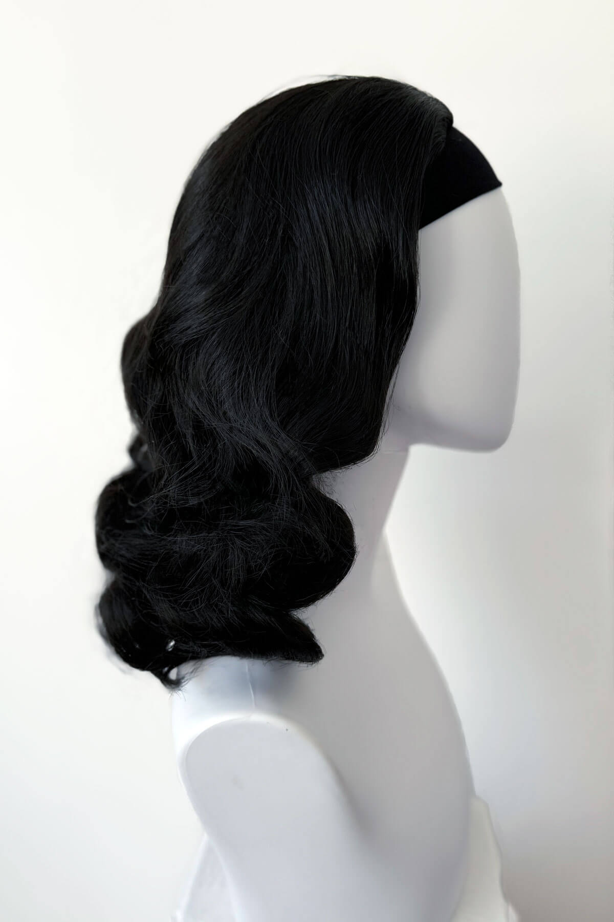 Black wig on a mannequin head against a white background. 1950s style shoulder length half wig hairpiece with beautiful vintage waves: Onyx colour black 1B