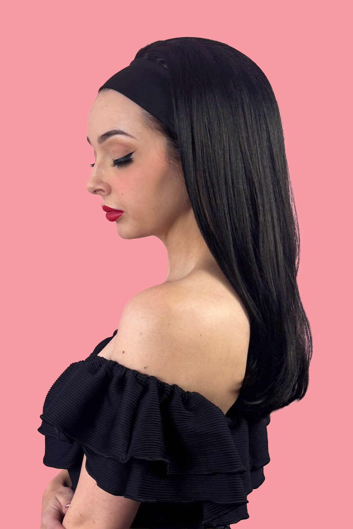 Woman with long black hair with a headband in it wearing a black off-shoulder top against a pink background. Headband half wig hairpiece, long and straight: Isla black 1B