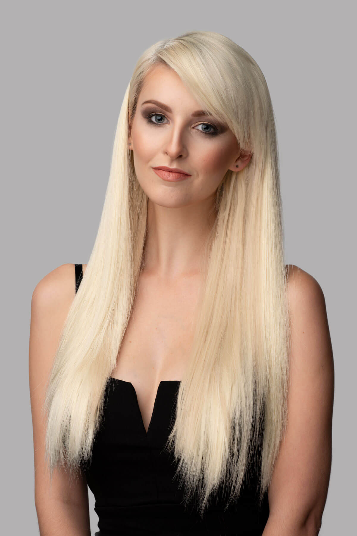 Woman with long blonde hair wearing a black top against a gray background. Straight blonde half wig hairpiece (3/4 wig): Tabitha blonde 613