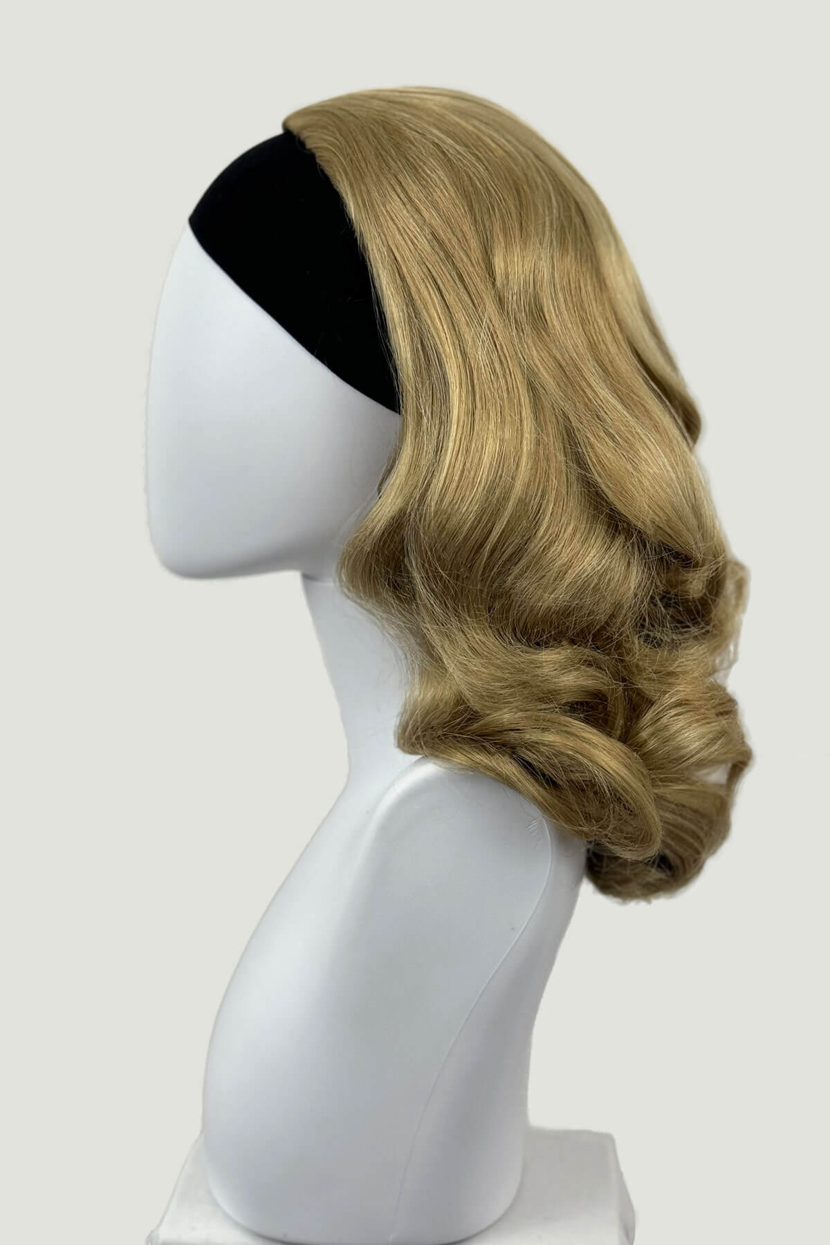 Blonde wig on a mannequin head against a white background shown from the side. 1950s style shoulder length half wig hairpiece with beautiful vintage waves: Onyx blonde 24H613 