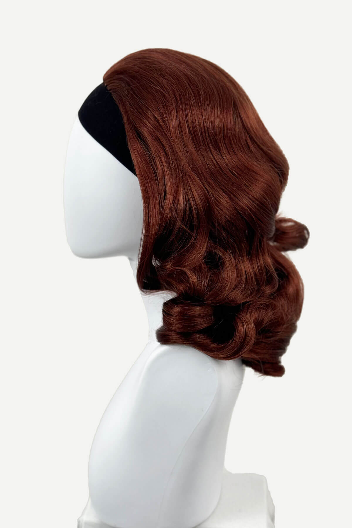 Brown wig on a white mannequin head against a white background, viewed  from the side. 1950s style shoulder length half wig hairpiece with beautiful vintage waves: Onyx copper red 130