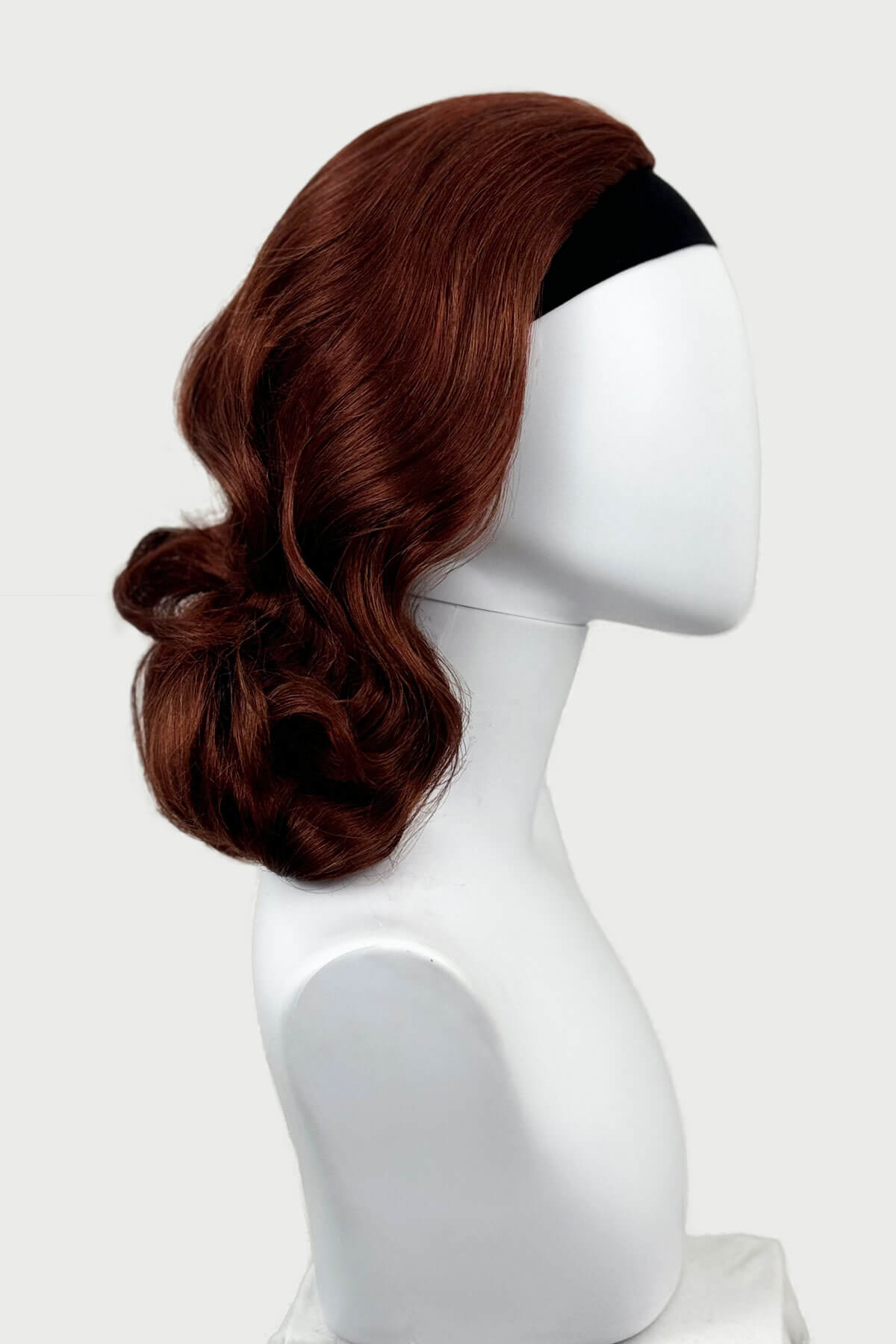 Brown wig on a white mannequin head against a white background, viewed  from the side. 1950s style shoulder length half wig hairpiece with beautiful vintage waves: Onyx copper red 130