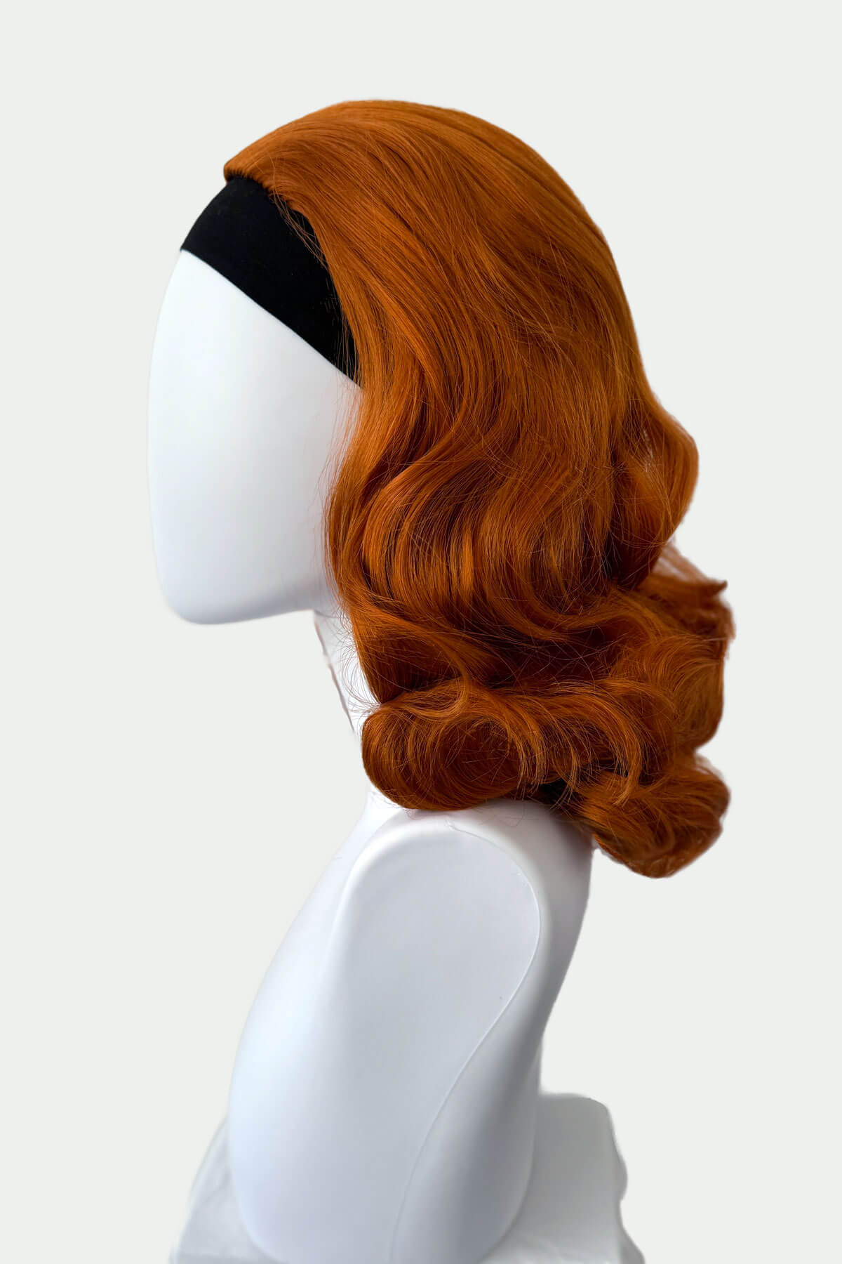 Ginger red wig on a mannequin head against a white background viewed from the side. 1950s style shoulder length half wig hairpiece with beautiful vintage waves: Onyx ginger