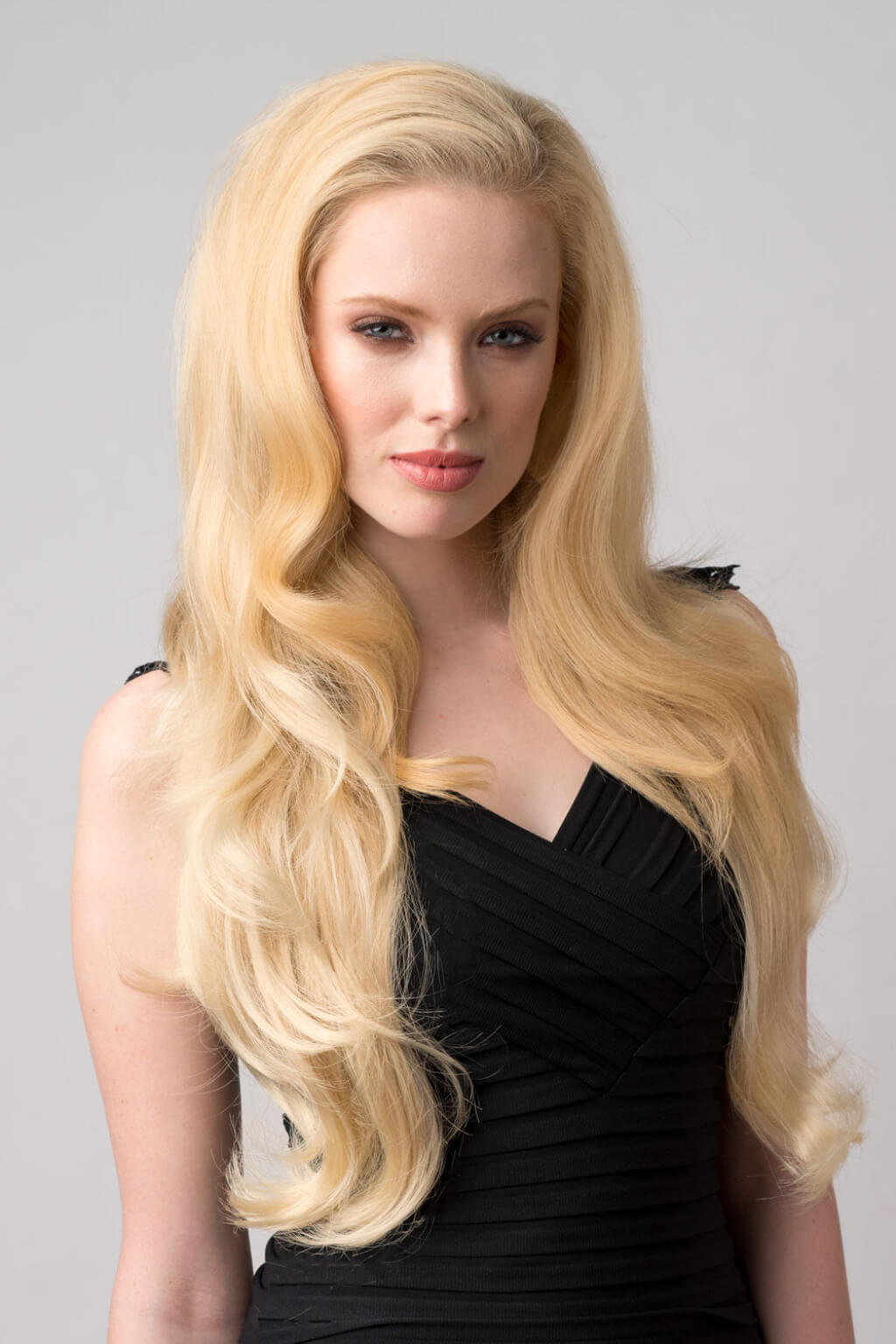Woman with long blonde hair wearing a black dress against a grey background. Suki - Super Full Volume, Extra Long, Bouncy Brown Half Wig blonde 24BH613