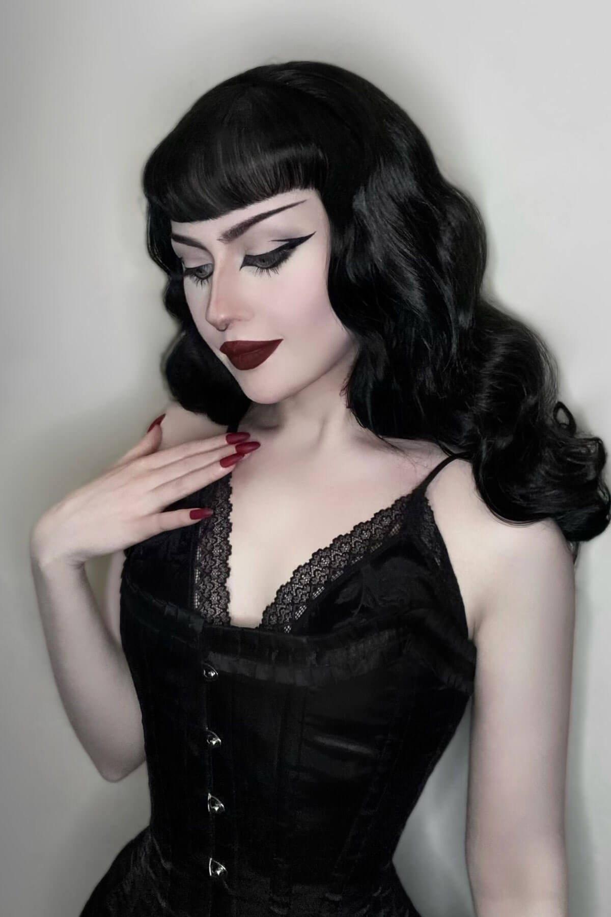 Woman wearing a black lace dress with a plain background. 1950s style half wig hairpiece with beautiful waves: Morgana jet black 