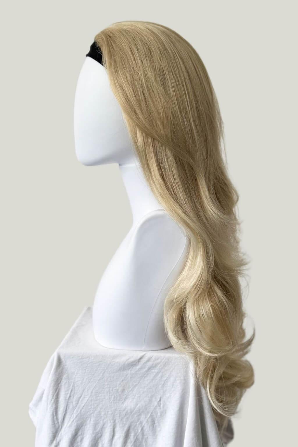 A long, wavy blonde wig displayed on a white mannequin head and shoulders against a light grey background. Blonde half wig hairpiece (3/4 wig), loose curls: Suki blonde 613T24