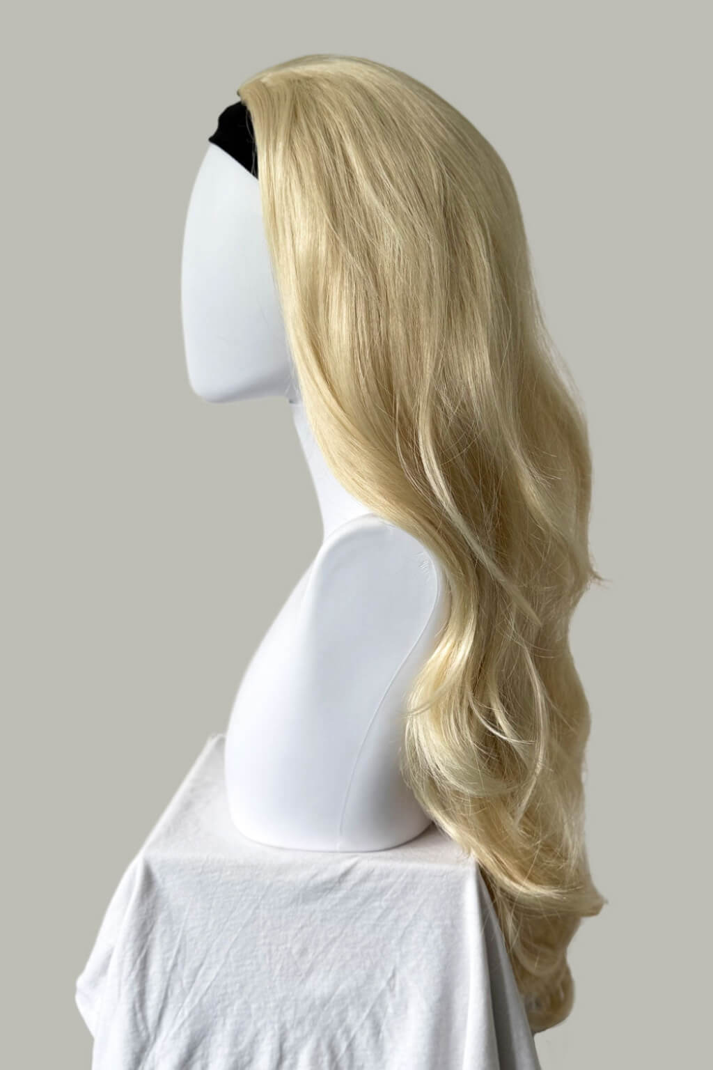 Blonde wig on a mannequin head against a plain background. Blonde half wig hairpiece (3/4 wig), loose curls: Suki creamy blonde 613