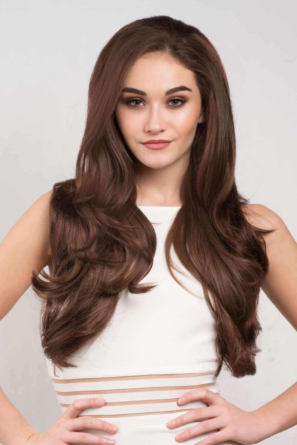 Woman with long brown hair wearing a white dress against a light gray background. Reddish-brown half wig hairpiece (3/4 wig) with big loose curls: Anne