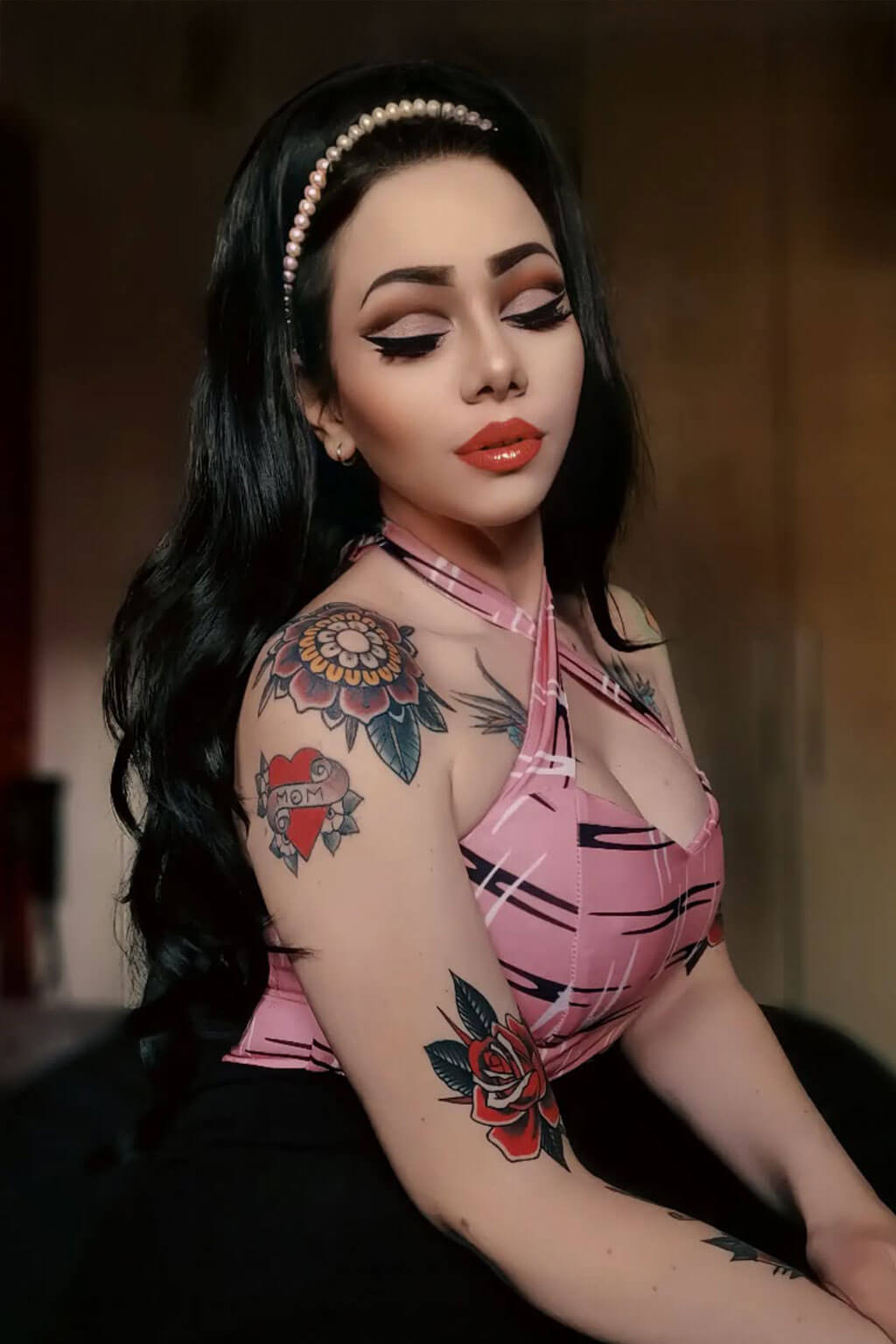 Woman with tattoos wearing a pink top against a blurred background. High crown long, wavy half wig and volume ring: Bardot jet black 1
